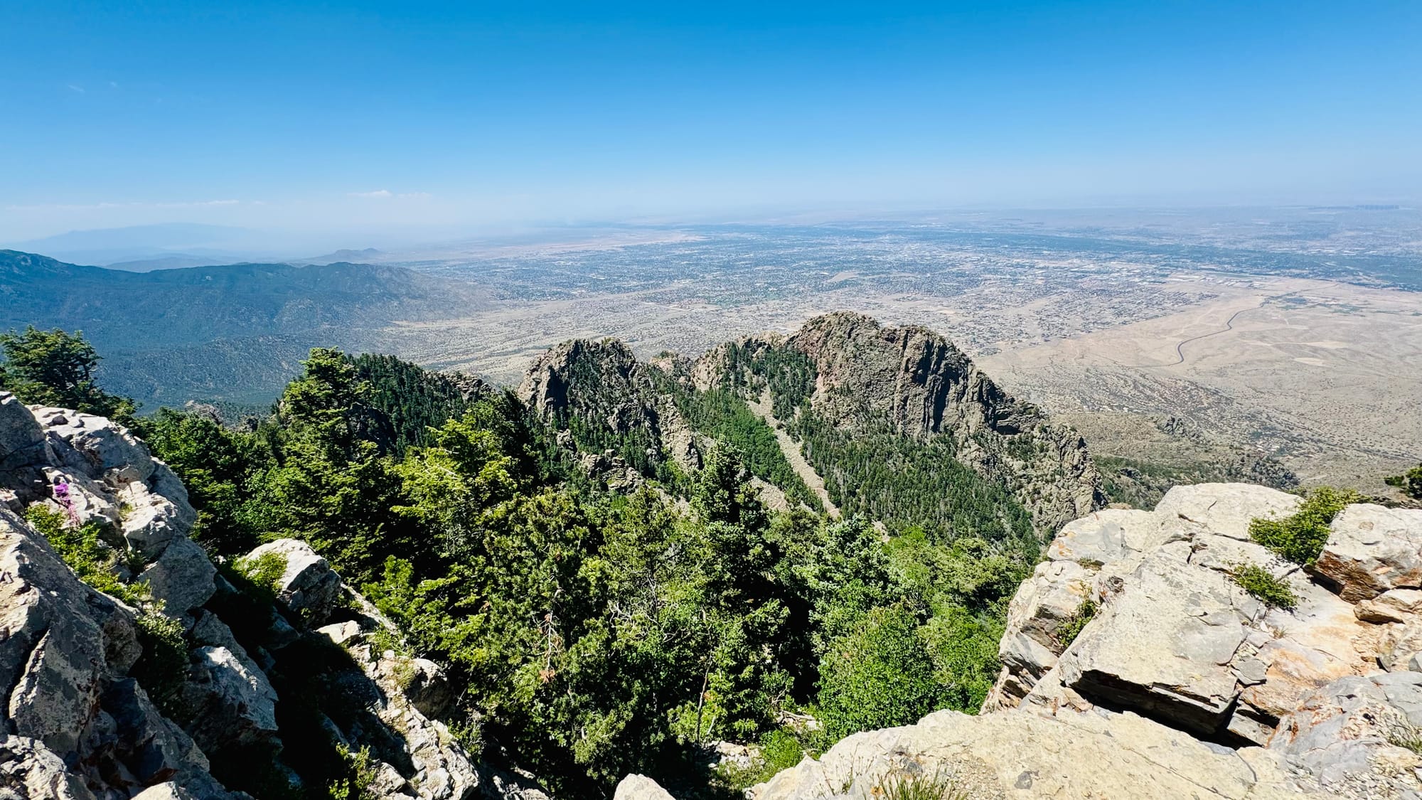 View intod a desert valley from a rocky outcrop under clear skies, with smoke in the distance.