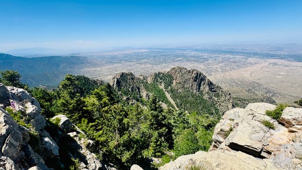 View intod a desert valley from a rocky outcrop under clear skies, with smoke in the distance.